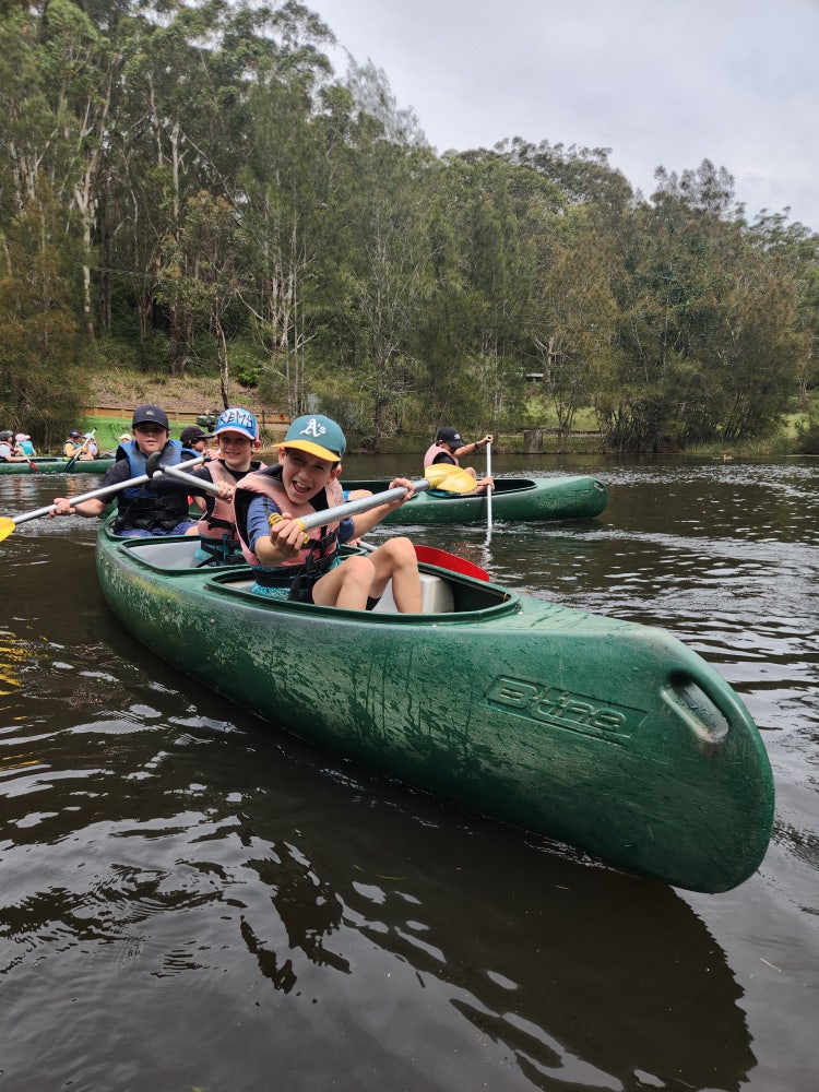 3 year 5 students in a green canoe in the water at the 2025 Great Aussie Bush Camp.