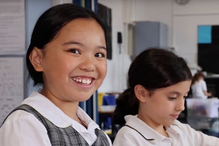 1 smiling girl student beside another girl student who is concentrating on her work.