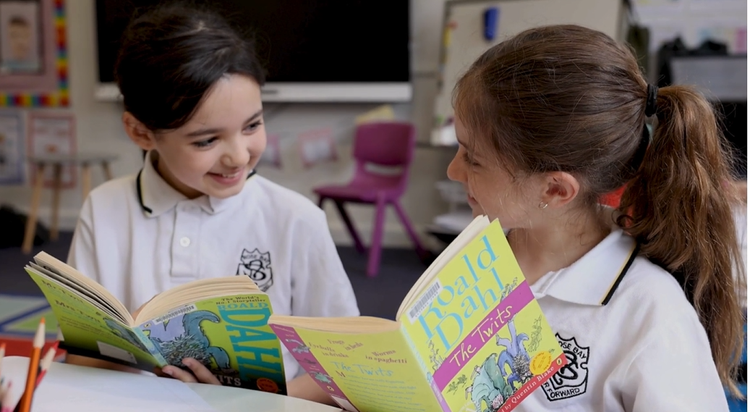 2 girl students reading Roald Dahl books in the library for the Premiers Reading Challenge