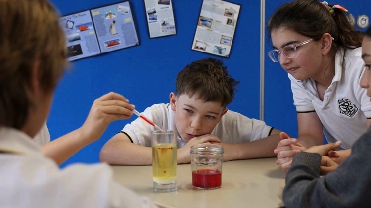 a group of students doing a science experiment with a beaker of red liquid and a beaker of yellow liquid.